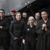 Group of the seven members of Belle & Sebastian. One female and the rest male, all dressed in dark clothing